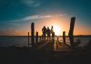 Group of friends silhouetted against a vibrant sunset on a wooden pier by the sea.