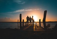Group of friends silhouetted against a vibrant sunset on a wooden pier by the sea.