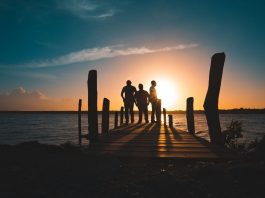 Group of friends silhouetted against a vibrant sunset on a wooden pier by the sea.