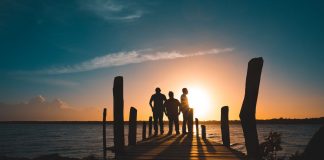 Group of friends silhouetted against a vibrant sunset on a wooden pier by the sea.