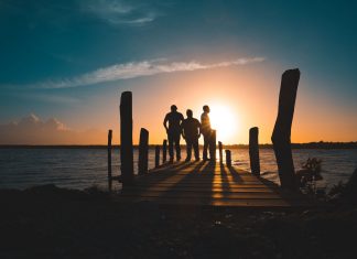 Group of friends silhouetted against a vibrant sunset on a wooden pier by the sea.