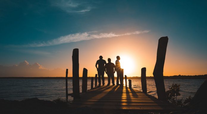 Group of friends silhouetted against a vibrant sunset on a wooden pier by the sea.