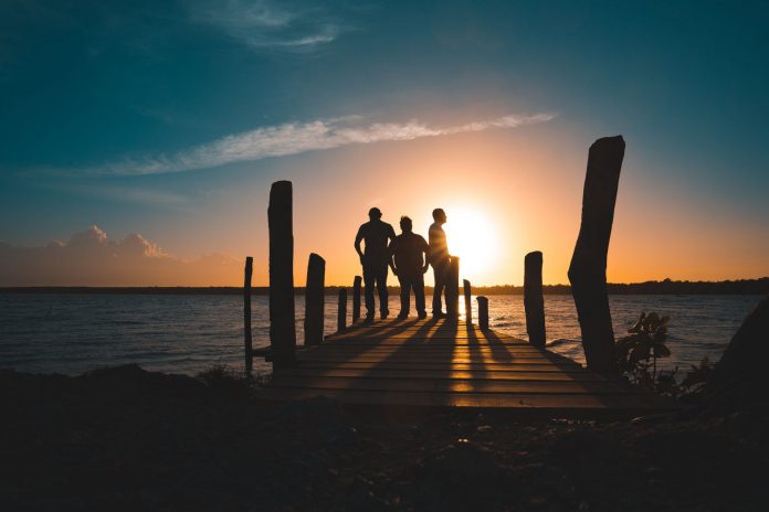 breaking-hoboken-yoga-event-returns-to-pier-a-june Group of friends silhouetted against a vibrant sunset on a wooden pier by the sea.