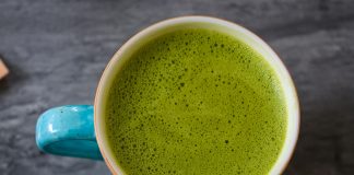 A top view of a ceramic cup filled with frothy green matcha latte on a dark surface.