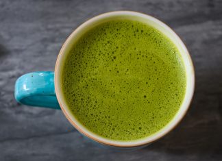 A top view of a ceramic cup filled with frothy green matcha latte on a dark surface.