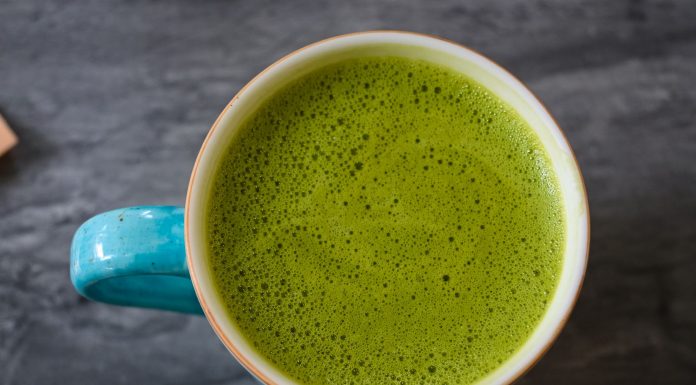 A top view of a ceramic cup filled with frothy green matcha latte on a dark surface.