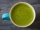 A top view of a ceramic cup filled with frothy green matcha latte on a dark surface.