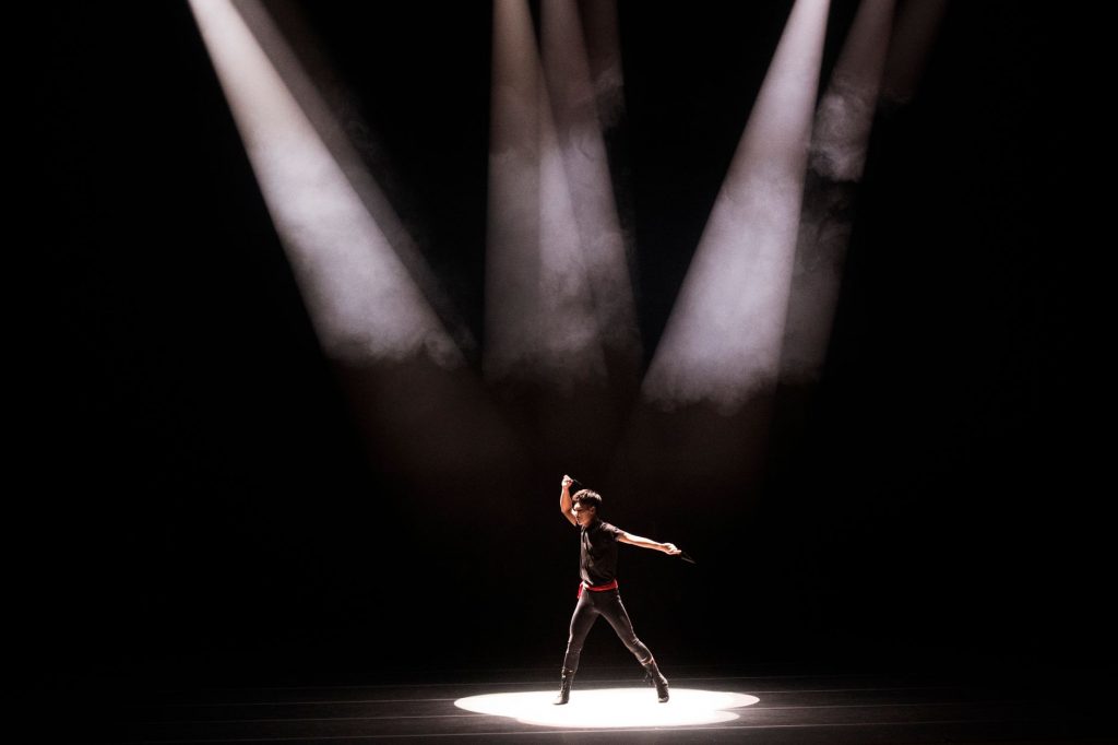 Energetic performance by male dancer under dramatic stage lighting.