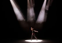 Energetic performance by male dancer under dramatic stage lighting.