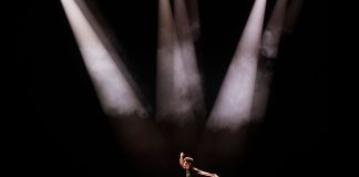 Energetic performance by male dancer under dramatic stage lighting.