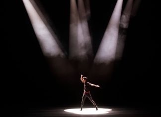 Energetic performance by male dancer under dramatic stage lighting.