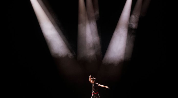 Energetic performance by male dancer under dramatic stage lighting.