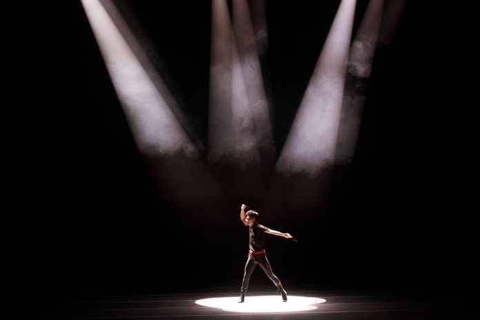 Energetic performance by male dancer under dramatic stage lighting.
