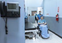 BREAKING: Jersey City Medical Center Sees Patient Surge After HUH Closure A nurse helps a patient in a wheelchair down a hospital corridor, reflecting care and medical professionalism.