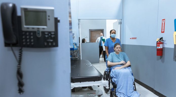 A nurse helps a patient in a wheelchair down a hospital corridor, reflecting care and medical professionalism.