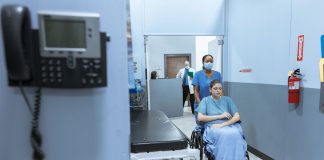 BREAKING: Jersey City Medical Center Sees Patient Surge After HUH Closure A nurse helps a patient in a wheelchair down a hospital corridor, reflecting care and medical professionalism.