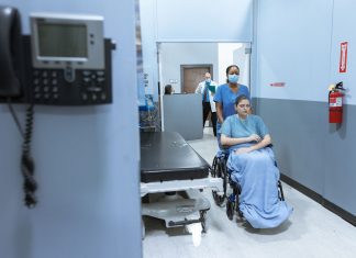 BREAKING: Jersey City Medical Center Sees Patient Surge After HUH Closure A nurse helps a patient in a wheelchair down a hospital corridor, reflecting care and medical professionalism.