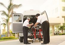BREAKING: Jersey City Medical Center Sees Surge in Patients After HUH Closure Two paramedics load medical equipment into a white ambulance outside a hospital in a tropical setting.