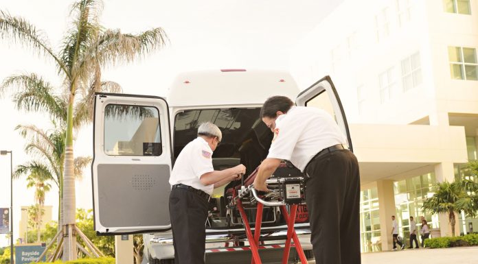 BREAKING: Jersey City Medical Center Sees Surge in Patients After HUH Closure Two paramedics load medical equipment into a white ambulance outside a hospital in a tropical setting.