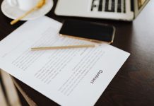 Close-up of a contract with office essentials like a laptop and coffee on a desk.