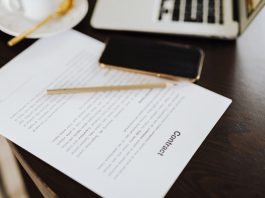 Close-up of a contract with office essentials like a laptop and coffee on a desk.