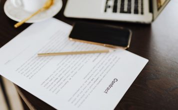 Close-up of a contract with office essentials like a laptop and coffee on a desk.