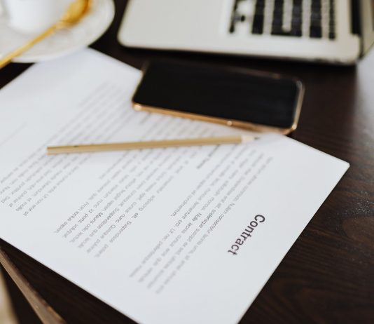 Close-up of a contract with office essentials like a laptop and coffee on a desk.