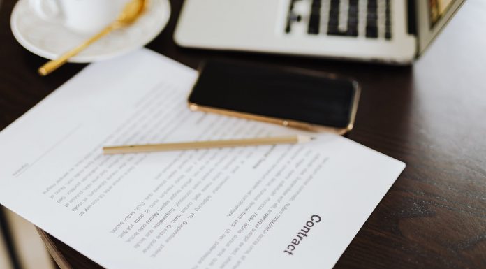 Close-up of a contract with office essentials like a laptop and coffee on a desk.