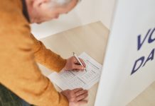 Senior man marking a ballot at a voting booth in an indoor polling station.