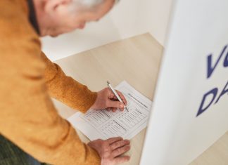 Senior man marking a ballot at a voting booth in an indoor polling station.