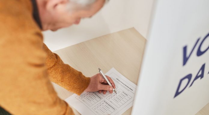 Senior man marking a ballot at a voting booth in an indoor polling station.