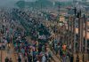 A bustling scene at a train station in Dhaka, Bangladesh with people crowding trains and platforms.