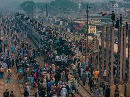 A bustling scene at a train station in Dhaka, Bangladesh with people crowding trains and platforms.