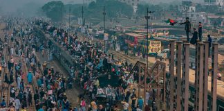A bustling scene at a train station in Dhaka, Bangladesh with people crowding trains and platforms.