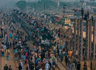 A bustling scene at a train station in Dhaka, Bangladesh with people crowding trains and platforms.