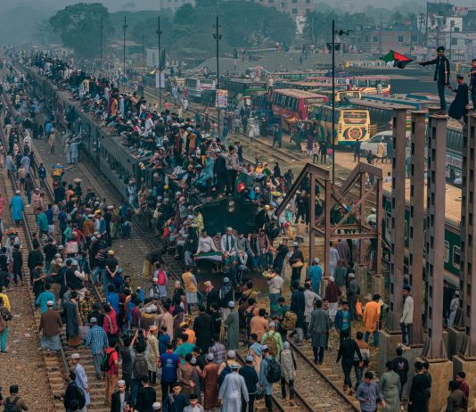 A bustling scene at a train station in Dhaka, Bangladesh with people crowding trains and platforms.