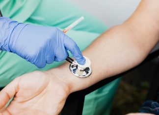 Healthcare professional using a stethoscope on patient's wrist during a medical exam.