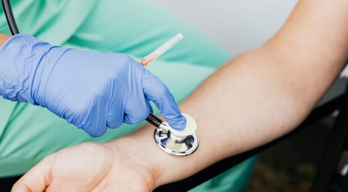 Healthcare professional using a stethoscope on patient's wrist during a medical exam.