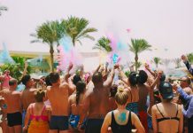 A lively outdoor Holi celebration on the beach with colorful powder and a joyful crowd.