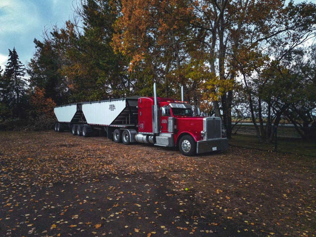 A red trailer truck parked outdoors surrounded by autumn trees in Purple Springs, Canada.