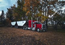 A red trailer truck parked outdoors surrounded by autumn trees in Purple Springs, Canada.