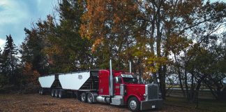 A red trailer truck parked outdoors surrounded by autumn trees in Purple Springs, Canada.