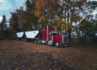 A red trailer truck parked outdoors surrounded by autumn trees in Purple Springs, Canada.