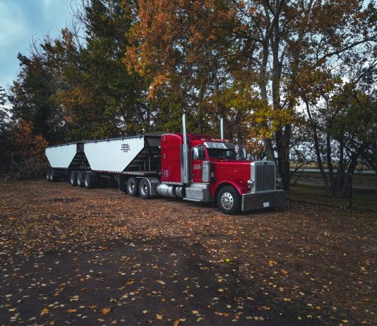 A red trailer truck parked outdoors surrounded by autumn trees in Purple Springs, Canada.