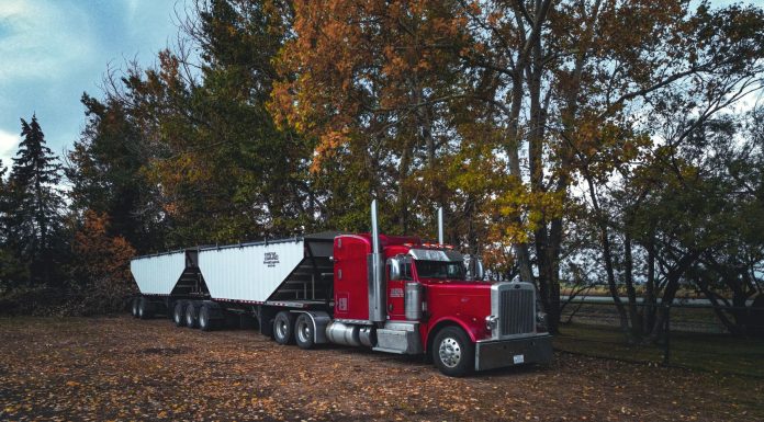 A red trailer truck parked outdoors surrounded by autumn trees in Purple Springs, Canada.