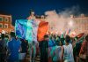 Vivid night-time celebration in France with crowds waving flags in city square.