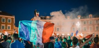 Vivid night-time celebration in France with crowds waving flags in city square.