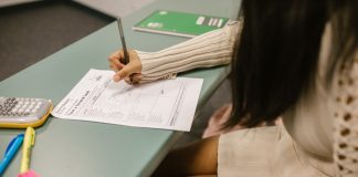Student secretly looking at a cheat sheet under the desk while taking an exam in a classroom setting.