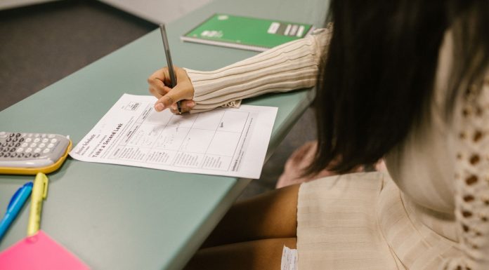 Student secretly looking at a cheat sheet under the desk while taking an exam in a classroom setting.