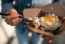 Close-up of a sunny side up egg in a takeout box being eaten with a fork.